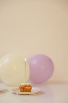 A single cupcake with a lit candle against a backdrop of pastel balloons.