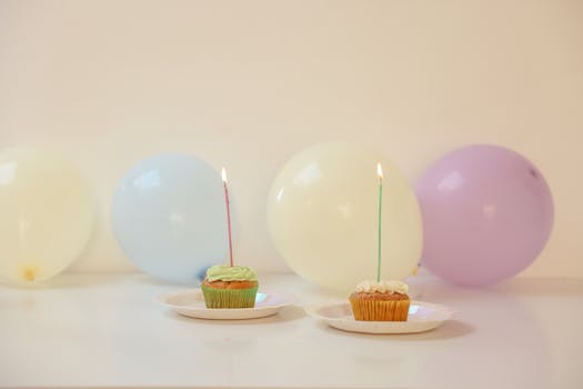 Vibrant cupcakes with lit candles surrounded by balloons, perfect for celebrations.