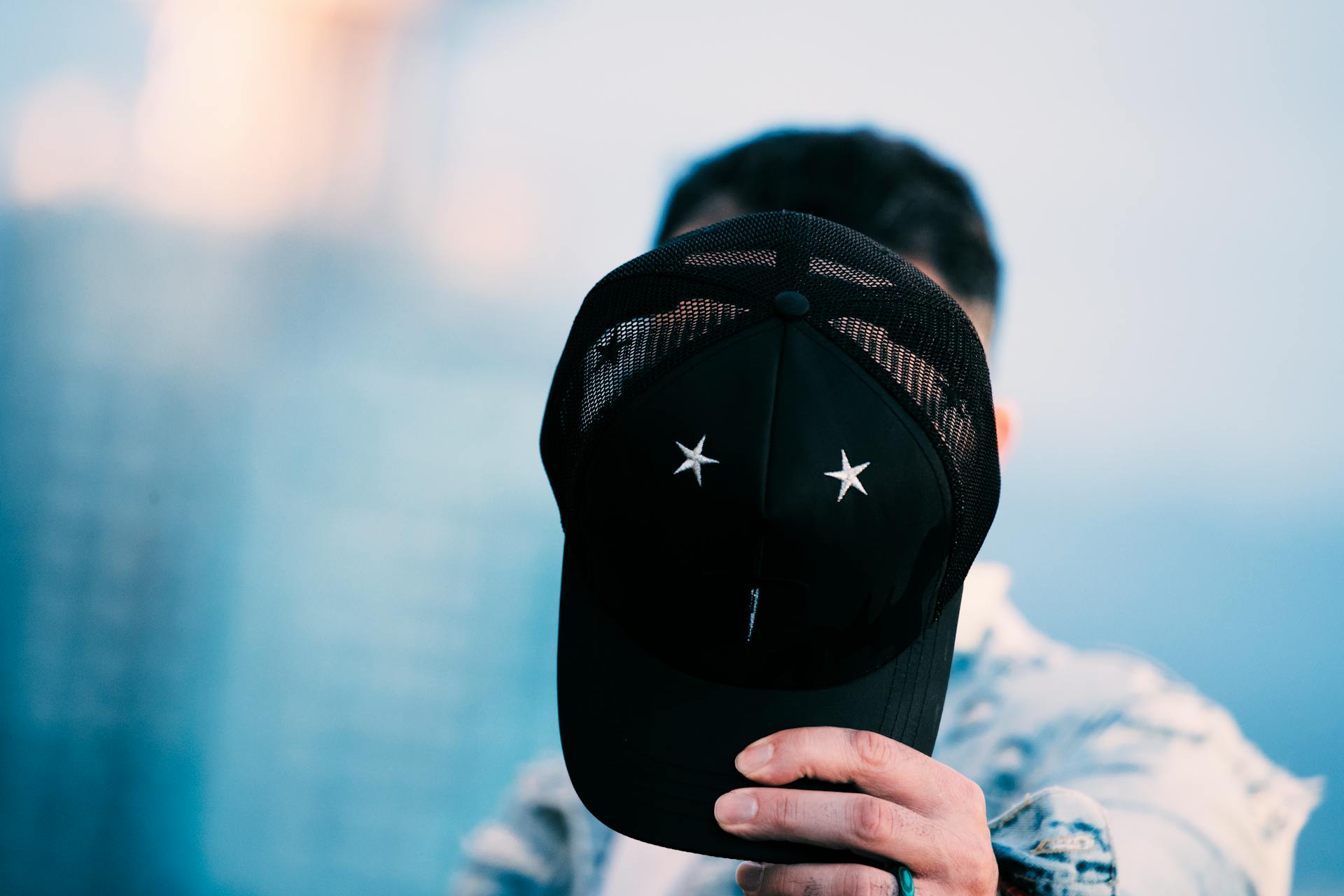 A close-up of a person holding a black cap with stars, representing anonymity and mystery.