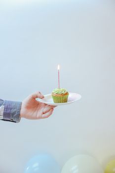 Celebratory cupcake with a lit candle on a plate against a soft background.