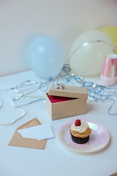 A birthday setup with a cupcake, gift box, balloons, and confetti, ideal for party themes.