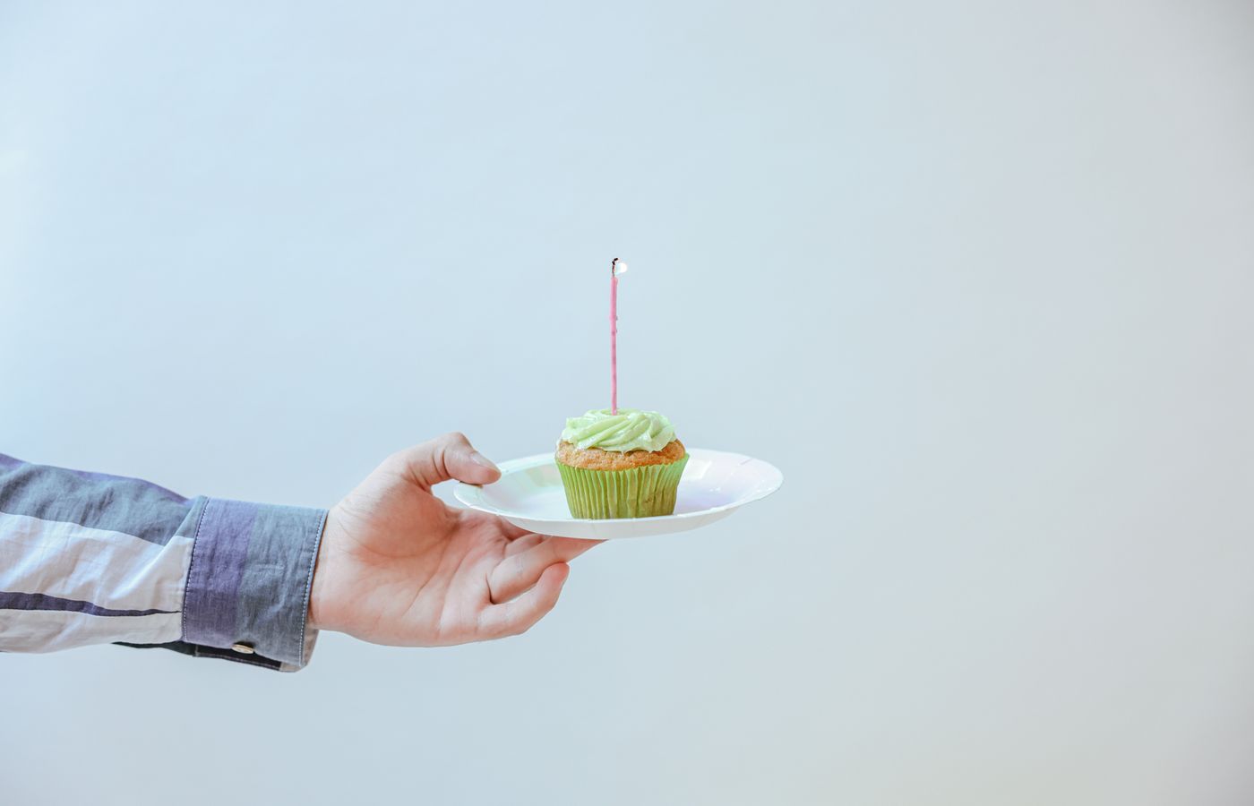 A single cupcake with a lit candle being held on a plate, perfect for celebrations.