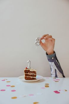 A slice of birthday cake with number candles on a festive table.