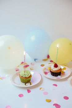 Colorful cupcakes with lit candles and balloons for a cheerful birthday celebration.
