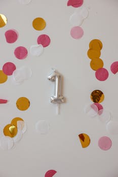Festive silver balloon number 1 surrounded by colorful confetti on a white background.