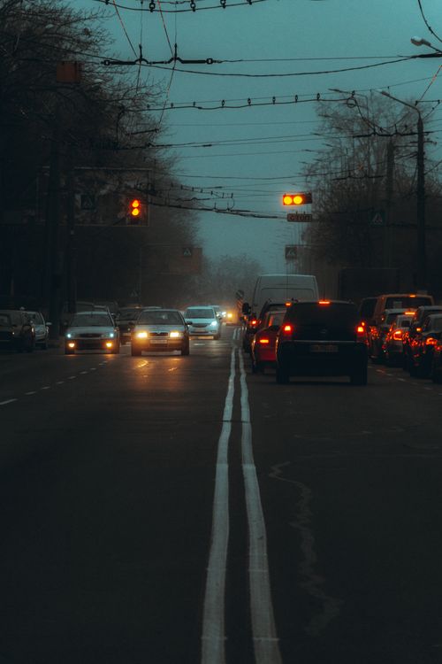 Free A moody street scene with cars and red traffic lights on a city road at dusk. Stock Photo