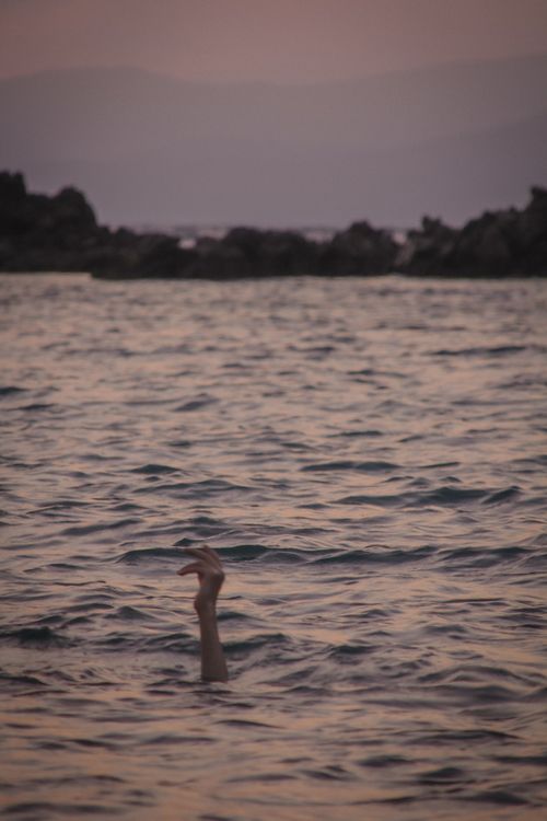 Free A hand reaches out from the ocean at dusk, creating a dramatic scene. Stock Photo