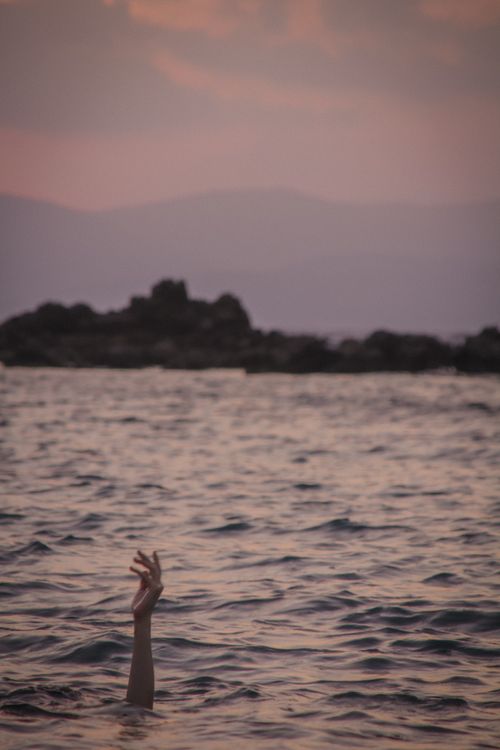 Free A hand emerges from the ocean at sunset, creating a dramatic and emotional scene. Stock Photo