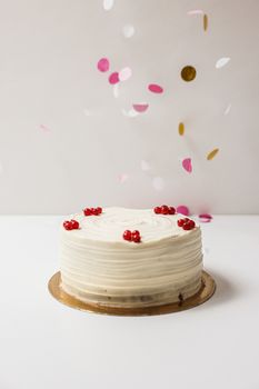 White frosted cake with berries and festive confetti falling against a neutral background.