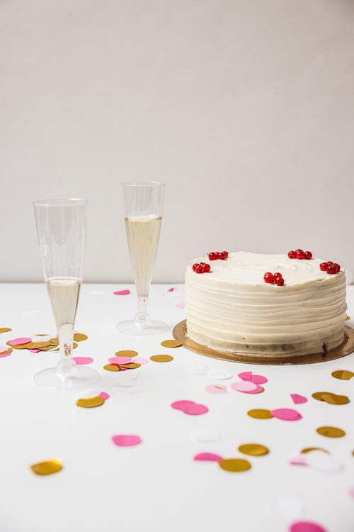 Free Elegant celebration setup with a cake, champagne, and colorful confetti on a white background. Stock Photo