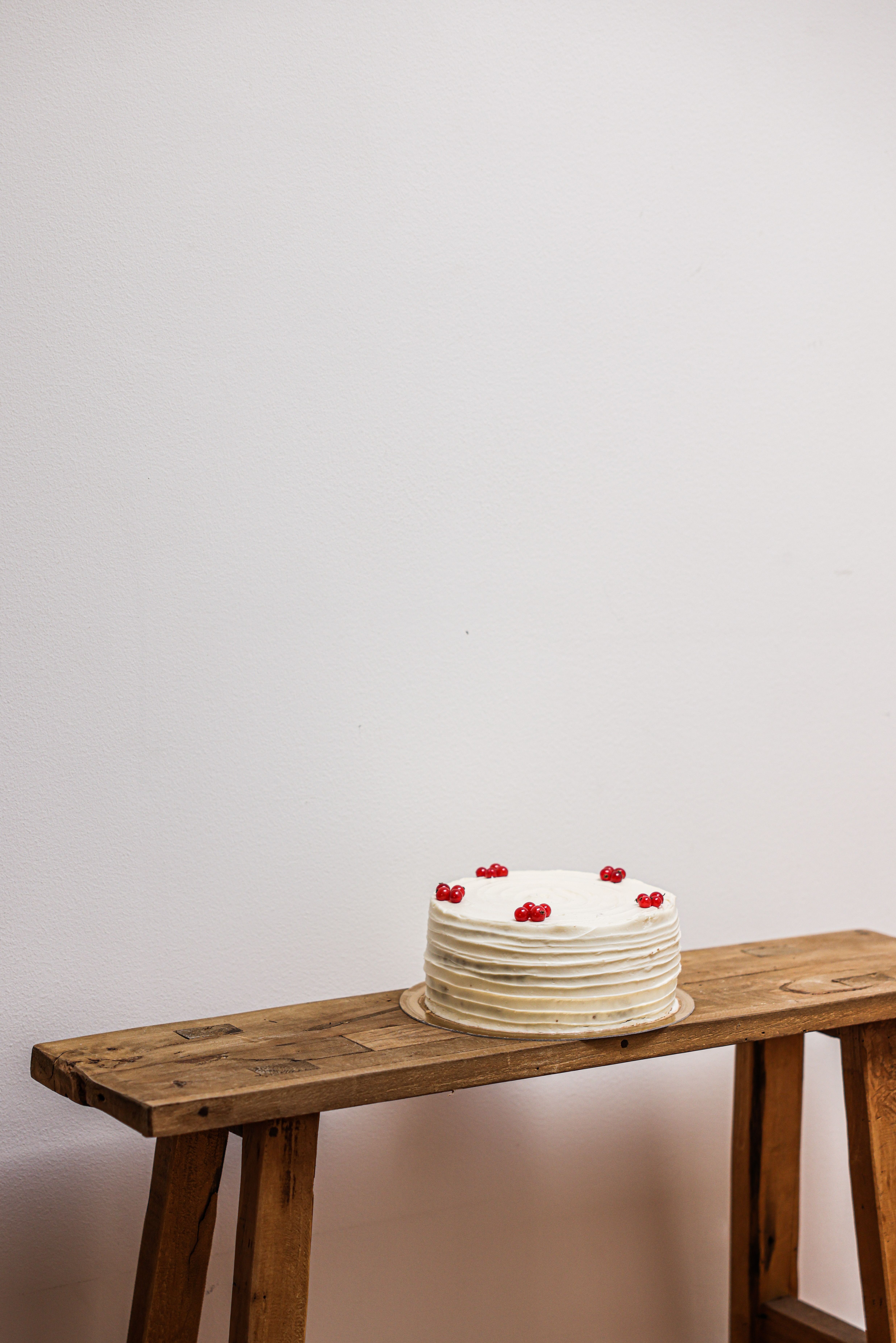 White cake decorated with berries on a wooden bench against a plain white wall.