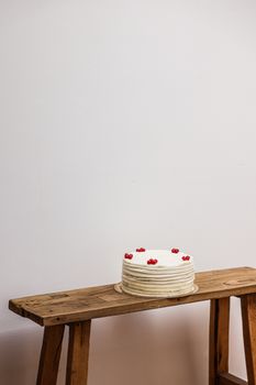 White cake decorated with berries on a wooden bench against a plain white wall.