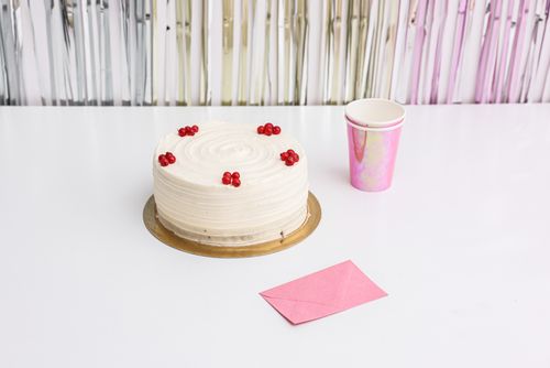 Free White cake with red berries, pink envelope, and cups on a festive table. Stock Photo