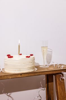 White cake on wooden table with candle and champagne, festive setup.