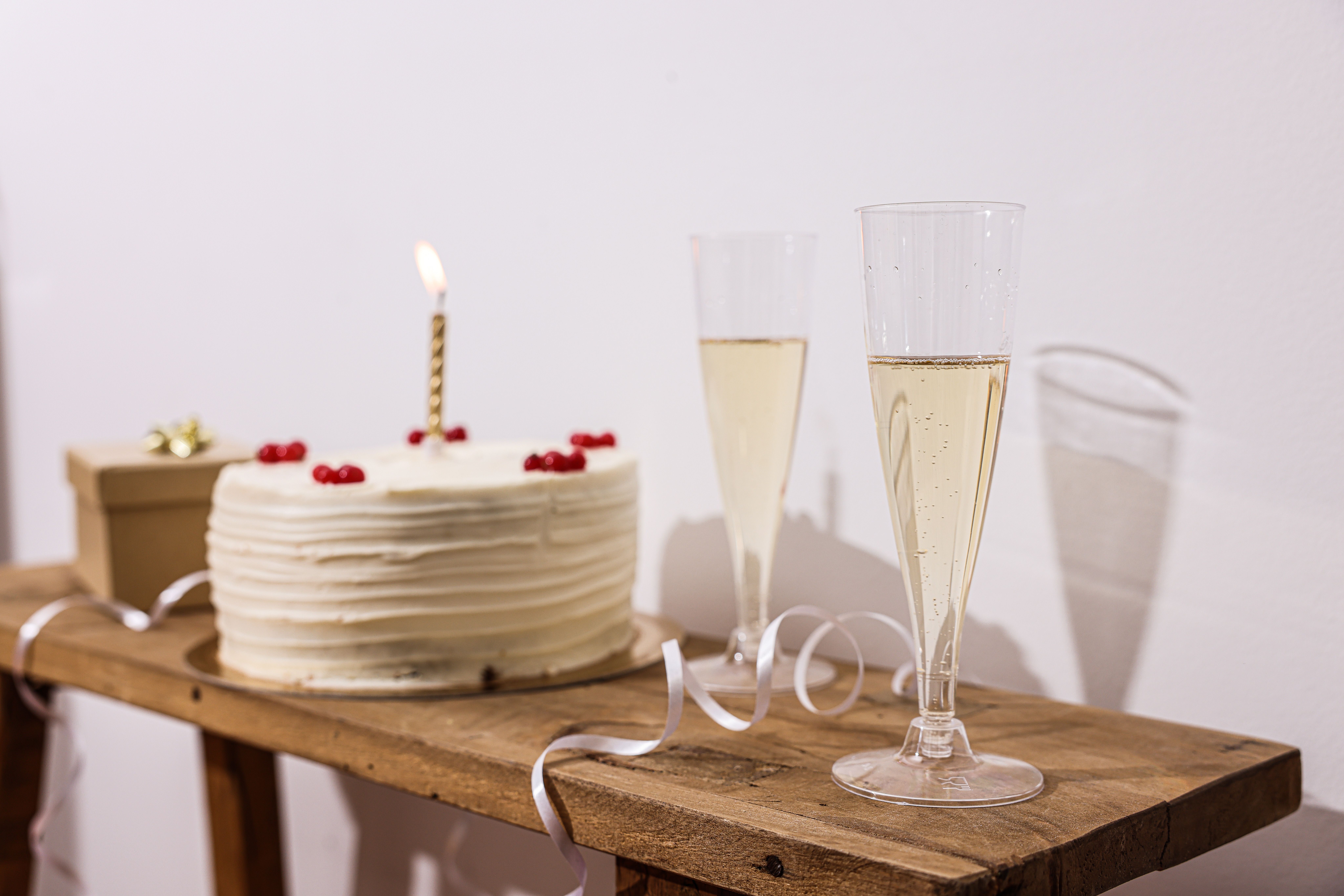 A beautifully iced cake with a single candle and champagne glasses set for celebration on a rustic table.