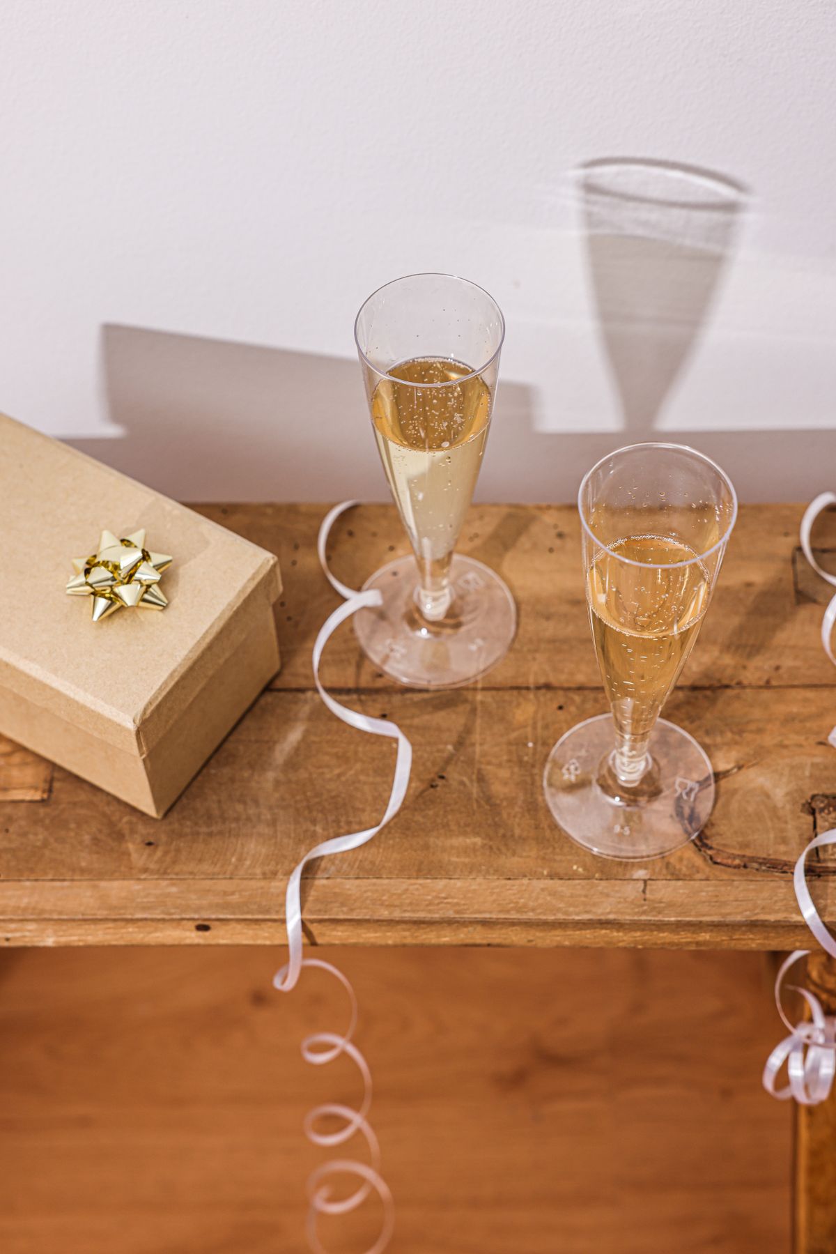 Two champagne flutes and a small wrapped gift box on a wooden table, the start of a simple Christmas drinks plan