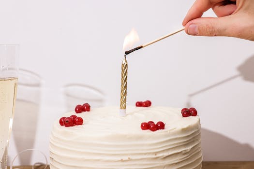 A hand lighting a candle on a white frosted berry-decorated cake, ideal for celebrations.