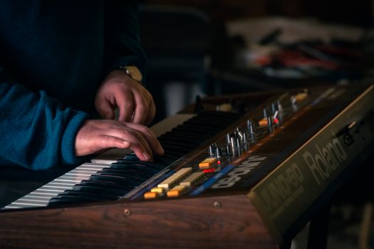 Hands playing a classic Roland Juno-60 synthesizer keyboard indoors, capturing a musical moment.