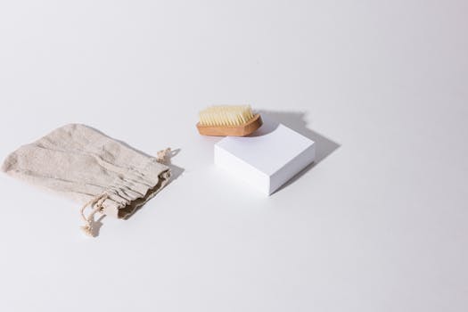Stylish minimalist product arrangement featuring a brush, box, and linen bag with shadows on a white background.