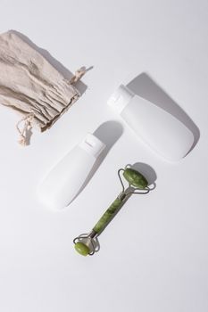 Flat lay of skincare bottles and jade face roller on a white background. Ideal for beauty concepts.