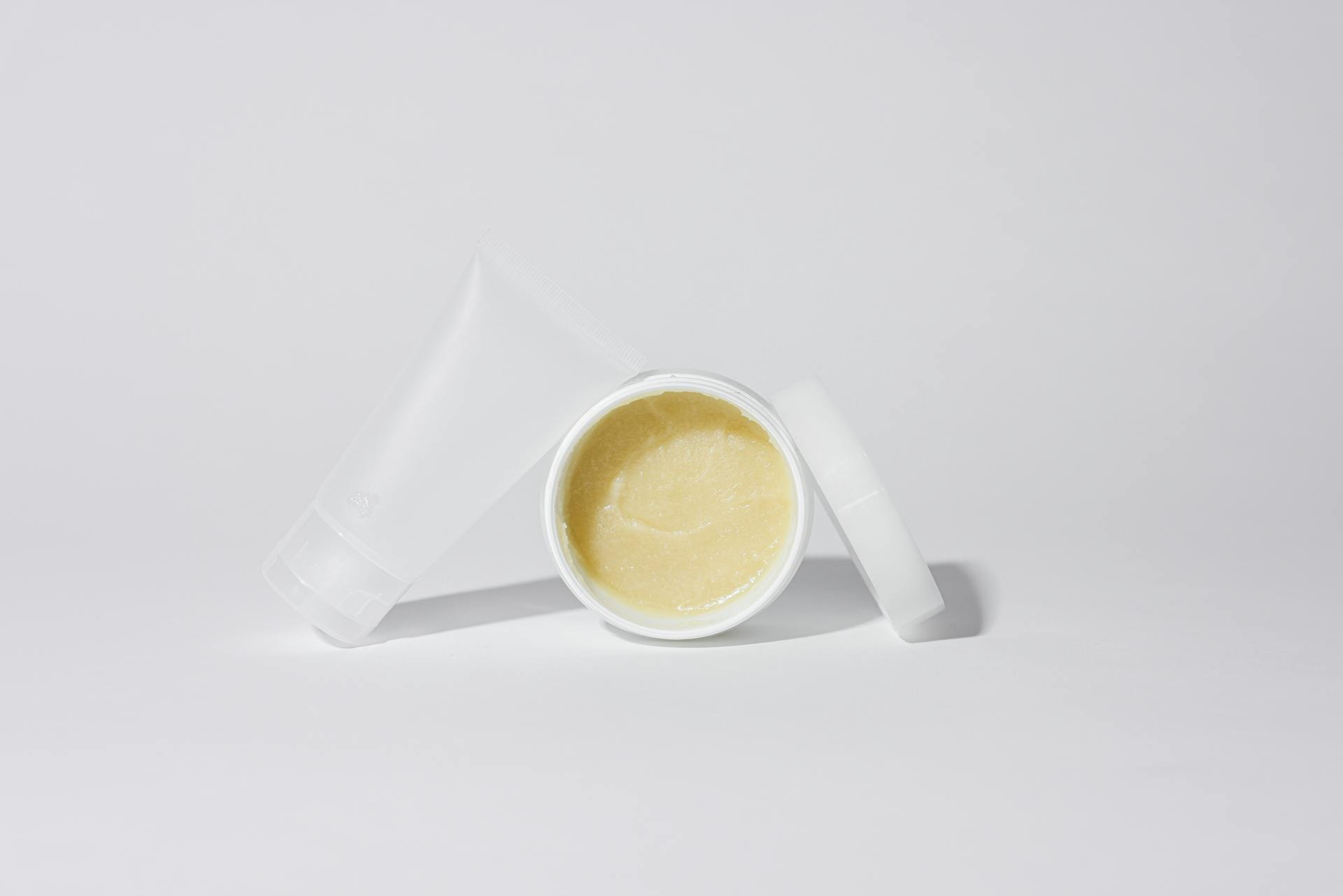 Studio shot of white plastic containers with yellow cream product on a white background.