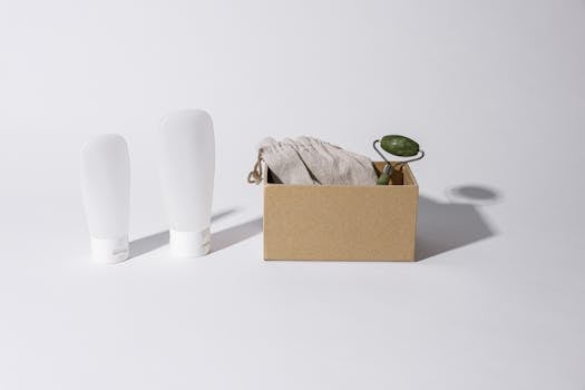 A minimalist setup of skincare essentials including a jade roller, cloth, and white bottles on a white surface.