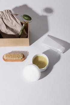 A flat lay photo featuring a jade roller, cream, brush, and pouch on a white background.