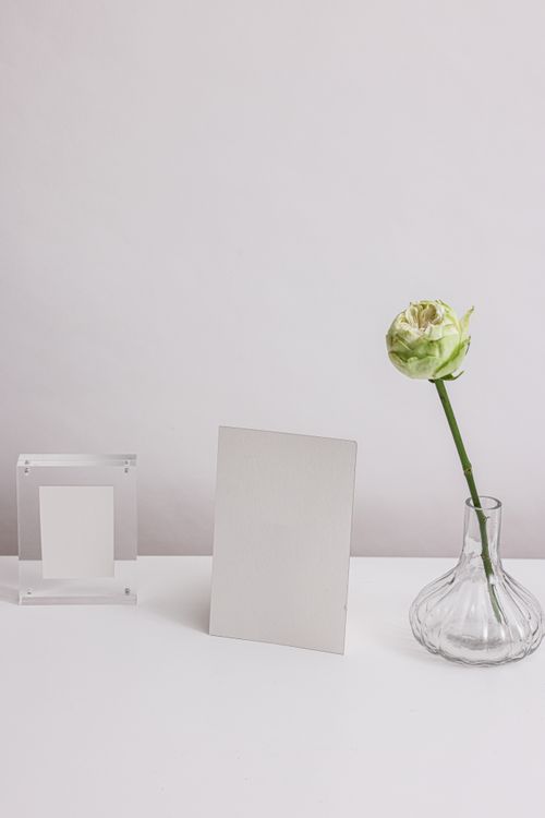 Free A simple and elegant still life arrangement with a blank card and a single white rose in a glass vase. Stock Photo