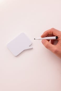 A close-up of a hand holding a pen near a speech bubble-shaped note pad.
