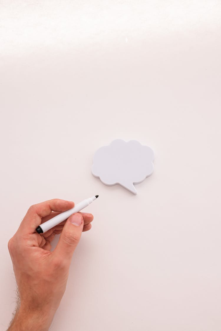 Person Holding A Pen Over A White Cloud Bubble Speech