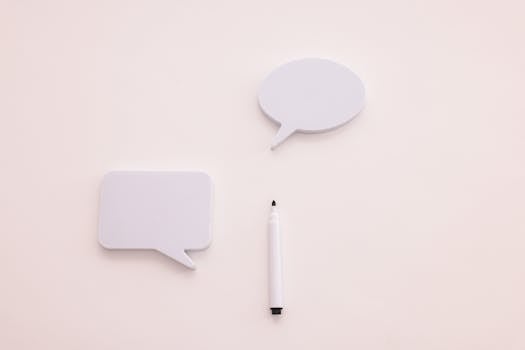 Minimalist image of two blank speech bubbles and a marker on a clean, white background.