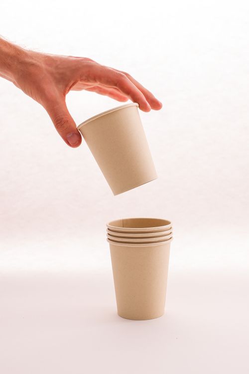 Free Close-up of a hand stacking biodegradable paper cups on a neutral background. Stock Photo