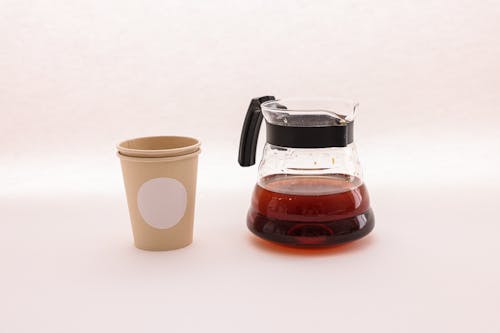 Paper Cups Beside a Glass Pitcher with Brown Liquid