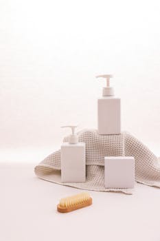 Cosmetic pump bottles and bath accessories arranged on a textured cloth with ample copy space.