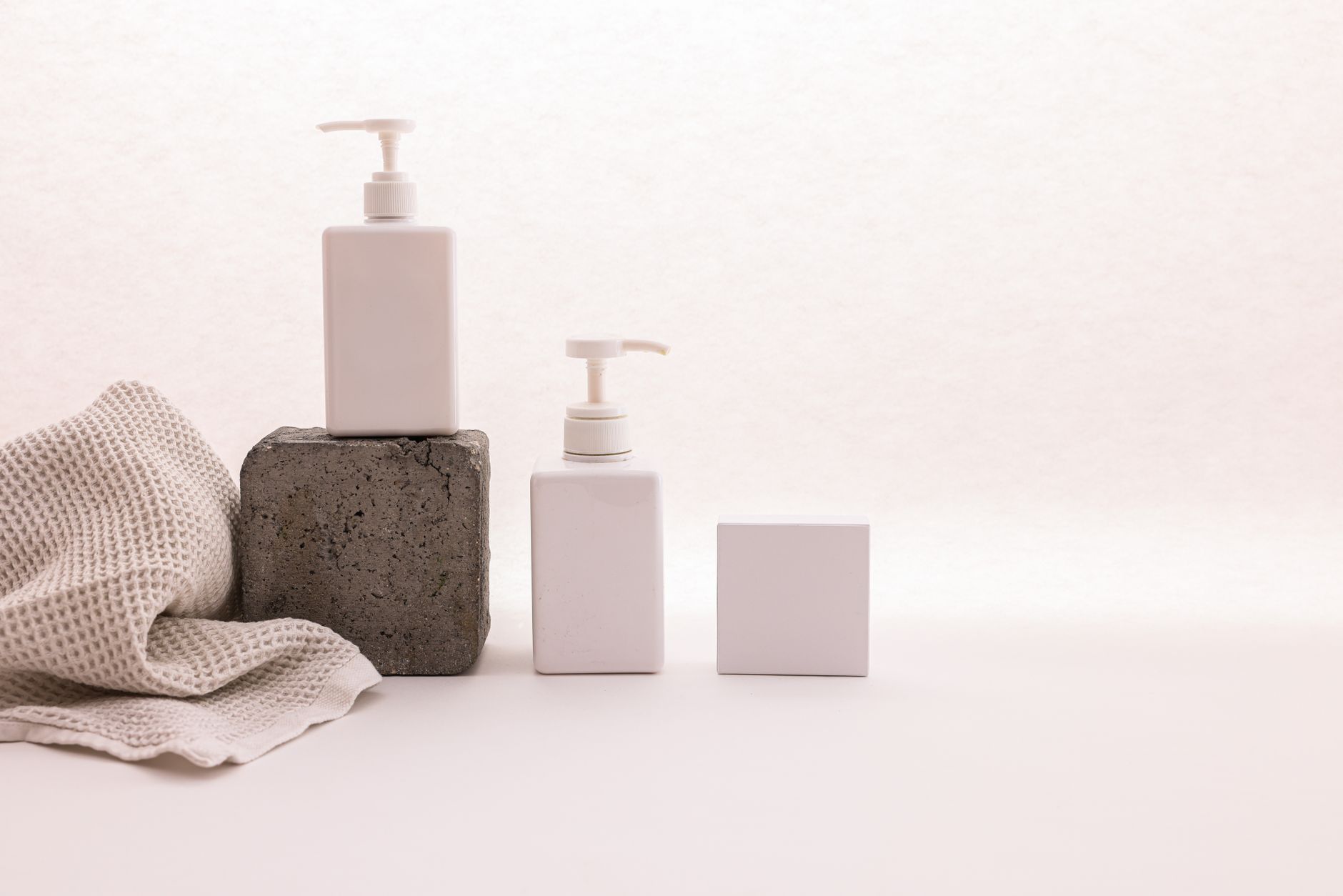 Stylish minimalist setup with cosmetic pump bottles and fabric on a white background, ideal for beauty product presentation..