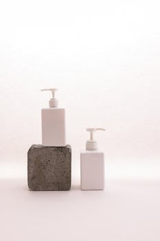 Minimalist still life featuring two white pump bottles on textured stone against a soft background.