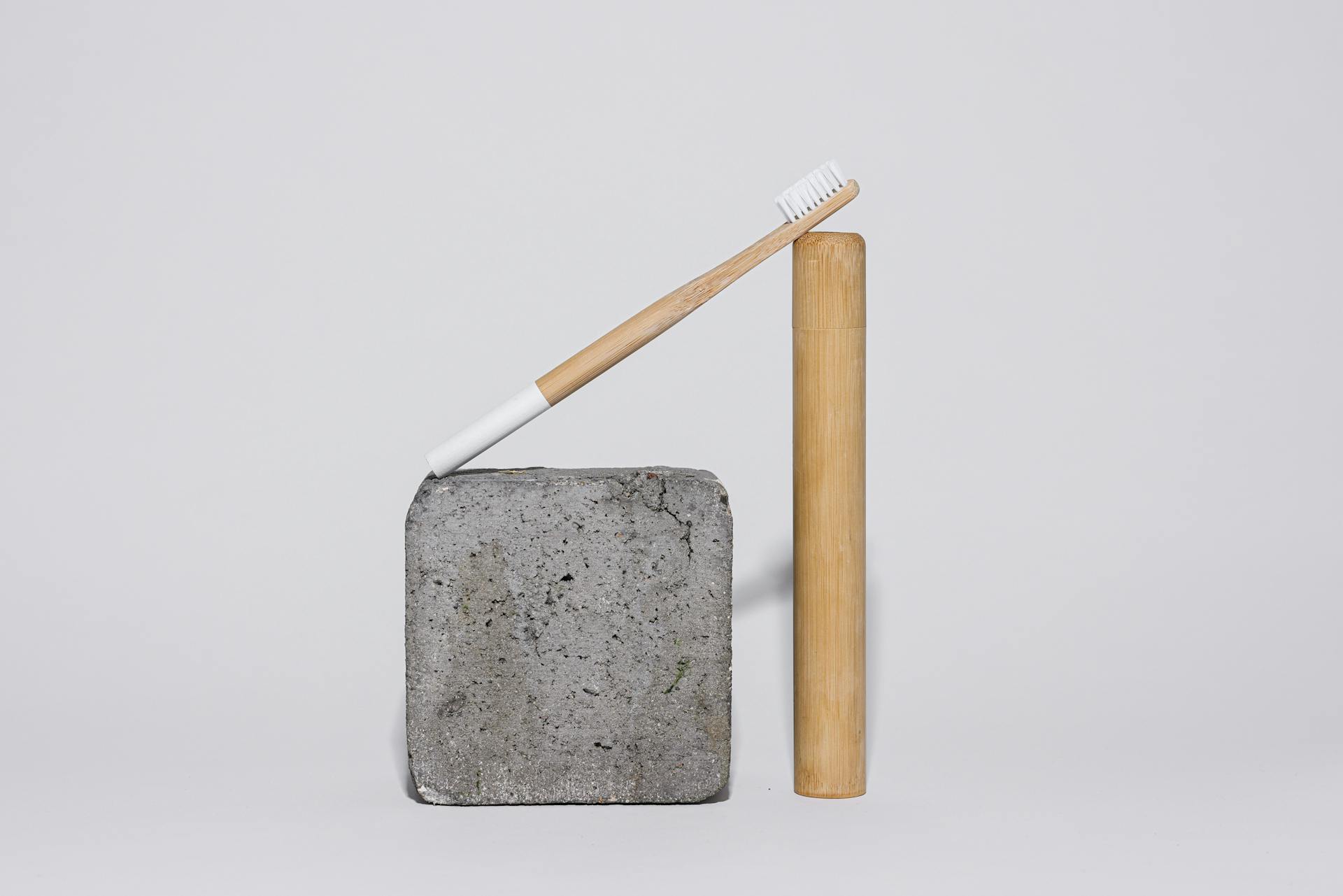 Eco-friendly bamboo toothbrush balanced on a concrete block and bamboo tube, showcasing modern simplicity.