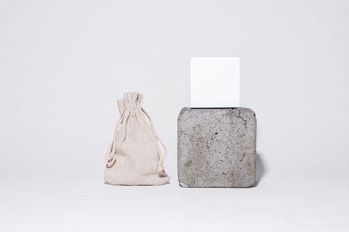Free A minimalist studio shot featuring a fabric bag and a stone cube against a white background. Stock Photo