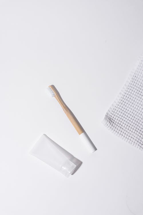 White Tube Cream Beside a Wooden Toothbrush
