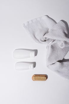 Flat lay of minimalist bathroom essentials with towel, bottles, and brush on white background.