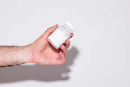 Free Close-up of a hand holding a small transparent plastic bottle against a bright white background. Stock Photo