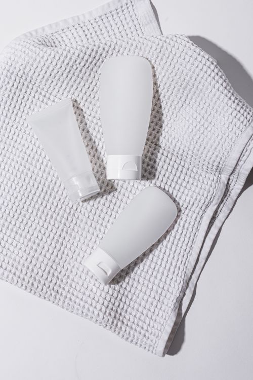Free Three white lotion tubes displayed on a textured cloth in a clean, minimalist setting. Stock Photo