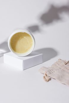 A white plastic jar of cream displayed on a box with soft shadows and a neutral background.