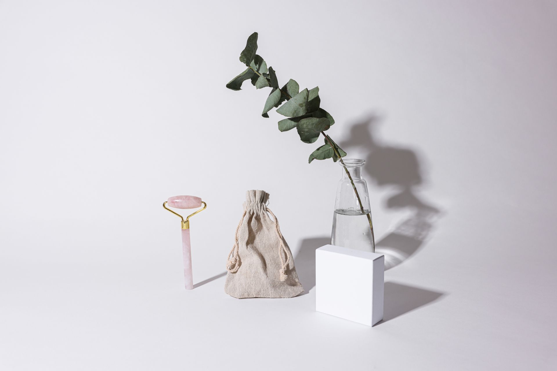 Elegant minimalistic setup featuring a jade roller, eucalyptus, and linen bag on a white background.