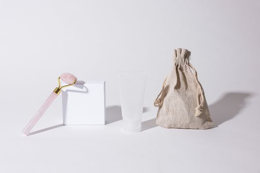 Cosmetic set with rose quartz roller and neutral packaging on white background.