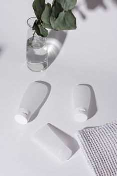 Elegant cosmetic squeeze tubes with foliage and towel on a white background.