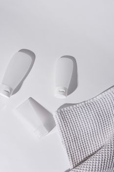 A clean and minimalist flat lay featuring skincare bottles and a towel on a white surface.
