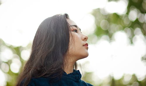 Free Artistic side portrait of a young woman amidst bokeh-filled greenery, capturing depth and elegance. Stock Photo