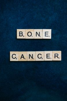 Wooden tiles spell 'Bone Cancer' on a dark blue background for medical awareness.