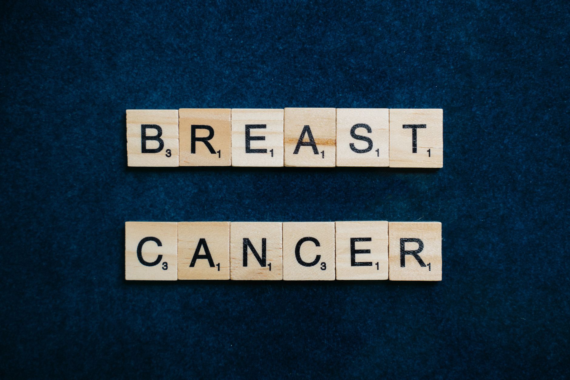 Wooden Scrabble tiles spelling 'Breast Cancer' on a dark blue background.